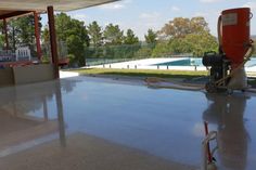 a concrete floor with a machine on it in front of a swimming pool and some trees