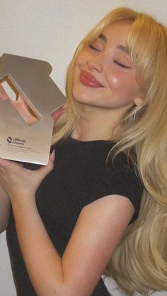 a woman is holding a box with her eyes closed and she has long blonde hair