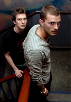 two young men standing next to each other on top of a stair case in front of a painting