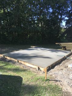 a large concrete slab in the middle of a field with benches and trees behind it