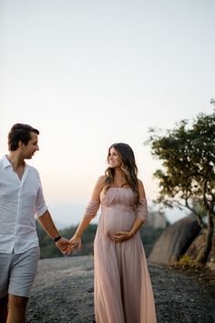 a pregnant woman holding the hand of her husband as they walk down a dirt road