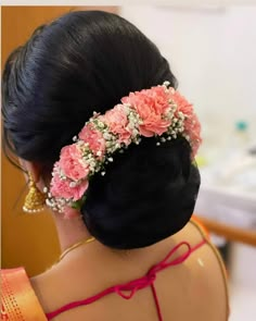 a woman with flowers in her hair is looking at the mirror and wearing an orange saree