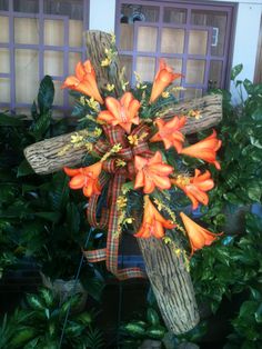 an arrangement of orange flowers in front of a wooden fence and door with green plants