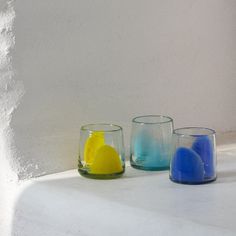 three different colored glasses sitting next to each other on a white counter top in front of a wall