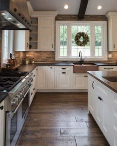 a kitchen with white cabinets and black counter tops, wood flooring and a wreath on the window sill