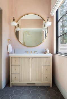 a bathroom with pink walls and a round mirror above the sink, along with two lamps