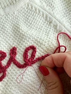 someone is stitching the word love in red yarn on a white knitted blanket