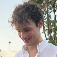 a man smiling and looking down at his cell phone in front of palm trees on the beach