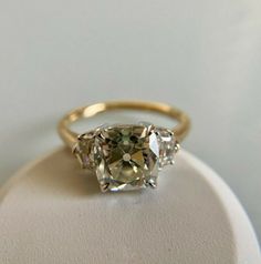 three stone ring sitting on top of a white display stand with an oval cut diamond in the center