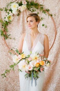 a woman in a white dress holding a bouquet of flowers next to a circular backdrop