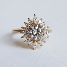 a diamond ring on a white surface with the center setting surrounded by smaller round diamonds