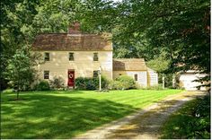 a white house with a red door sitting in the middle of a lush green field