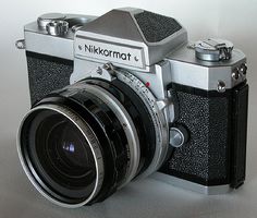 an old camera sitting on top of a white table next to a black and silver lens