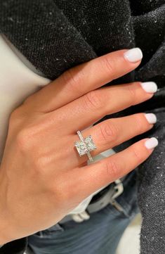 a woman's hand wearing a ring with a cross on the middle and white nails