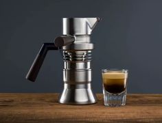 an espresso machine next to a shot glass on a wooden table with a gray background