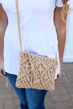 a woman carrying a crocheted bag on her shoulder and wearing blue jeans, white t - shirt