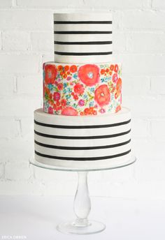 a multi - tiered cake decorated with flowers and black stripes on a white stand