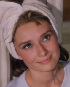 a woman with a towel wrapped around her head smiling at the camera while wearing a white shirt and blue eyeshadow