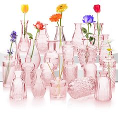 there are many pink vases with flowers in them on the white table and one is empty