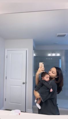 a woman holding a baby taking a selfie in front of a mirror with her phone