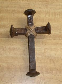 an old rusty metal cross hanging on a wooden wall with a rope attached to it