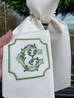 a hand holding a white cloth with green embroidery on it and a bow tie around the neck