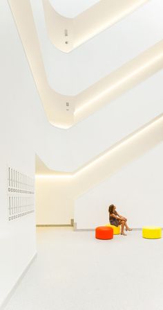 a woman sitting on an orange and yellow chair in a large room with white walls