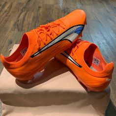 an orange pair of shoes sitting on top of a piece of paper in front of a wooden floor