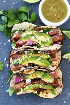 three steak tacos with avocado and cilantro sauce on the side