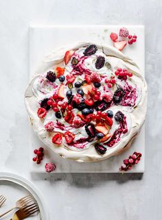 a white plate topped with a dessert covered in berries and whipped cream on top of a table