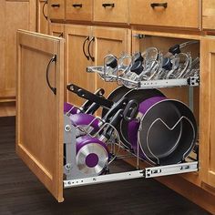 an open cabinet with pots and pans in it on the bottom shelf next to wooden cabinets