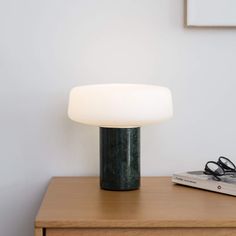 a table lamp sitting on top of a wooden dresser next to a book and eyeglasses