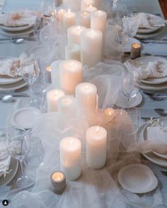 the table is set with white candles and plates for dinner guests to sit down at