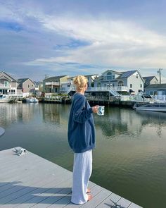 a woman standing on a dock holding a coffee cup in her hand and looking out over the water