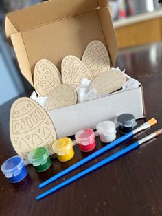 an open box filled with paints and paper cutouts on top of a wooden table