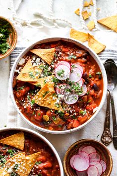 two bowls filled with chili and tortilla chips on top of a white table