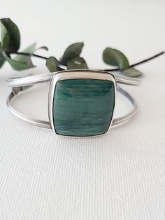 This large square Larsonite* is a deep sea-green color with darker greens sweeping across its surface. Simply set atop a cuff bracelet, the curving lines of silver give this statement cuff an elegant, feminine style. On the underside of the stone, waves of silver are cut away to reveal the beautiful underside of this u Modern Green Cuff Bangle Bracelet, Modern Green Cuff Bracelet As Gift, Modern Green Cuff Bracelet Gift, Modern Green Cuff Bracelet For Gift, Handmade Green Cuff Bracelet For Formal Occasions, Elegant Feminine Style, Sea Green Color, Green Jasper, Elegant Feminine