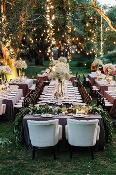 an outdoor dinner table set up with white flowers and greenery on the tables, surrounded by string lights