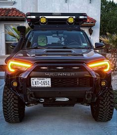 the front end of a black truck parked in front of a house with its lights on