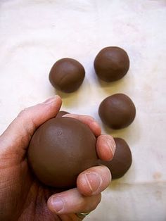 a hand holding a chocolate ball in front of several smaller ones on a table top