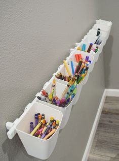 three white bins with pencils and markers on them are hanging from the wall