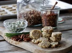 a wooden cutting board topped with lots of food next to glass containers filled with nuts