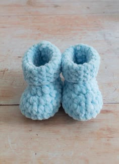 a pair of blue crochet baby booties sitting on top of a wooden floor