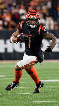 a football player running with the ball in his hand and wearing an orange helmet on