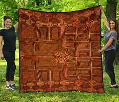 two women standing in the grass holding up a large brown and red blanket with circles on it