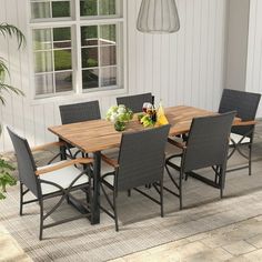 an outdoor dining table and chairs set up in front of a white house with large windows