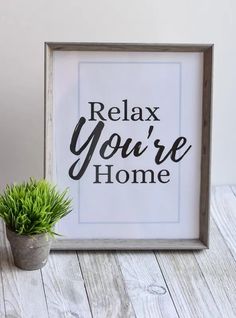 a framed sign that says relax you're home next to a potted plant