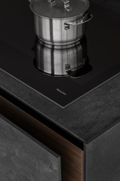 a pot is sitting on top of a stove with a black surface and wooden drawers