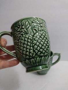 a hand holding a green coffee cup with an intricate design on it's side