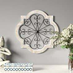 a decorative wall clock mounted to the side of a gray wall next to a vase with white flowers